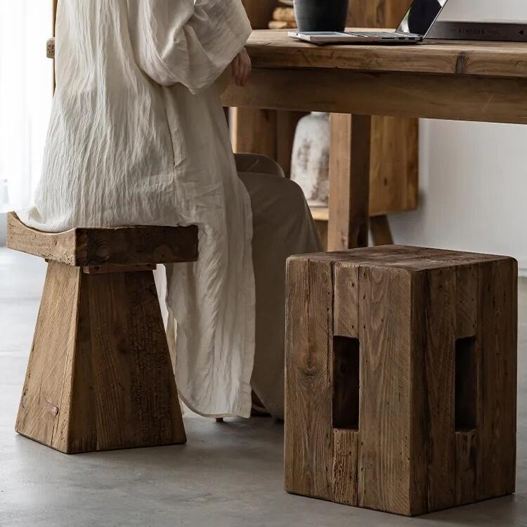 Woman sitting at wooden table in japandi dining room, with two stools and vase with plant